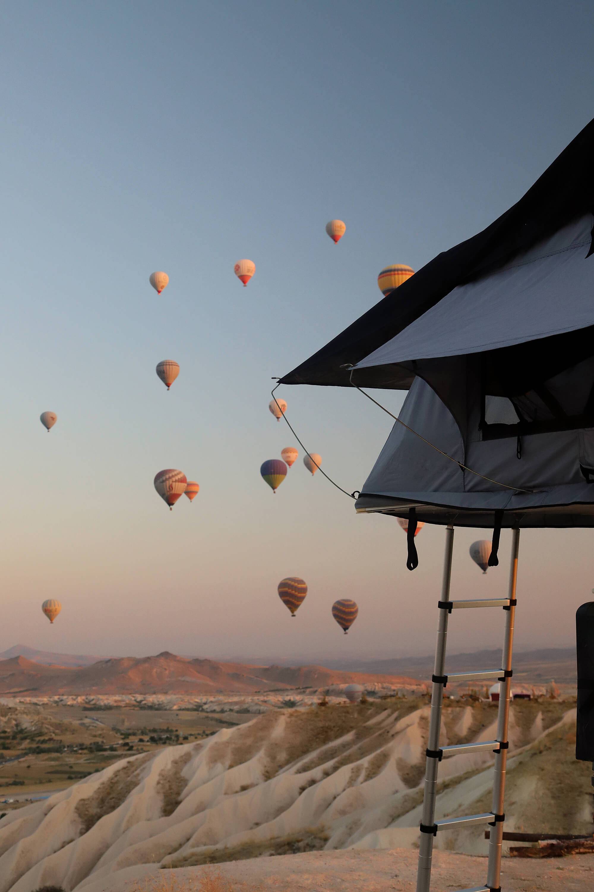 Dachzelt mit Leiter vor Himmel voller Heißluftballons