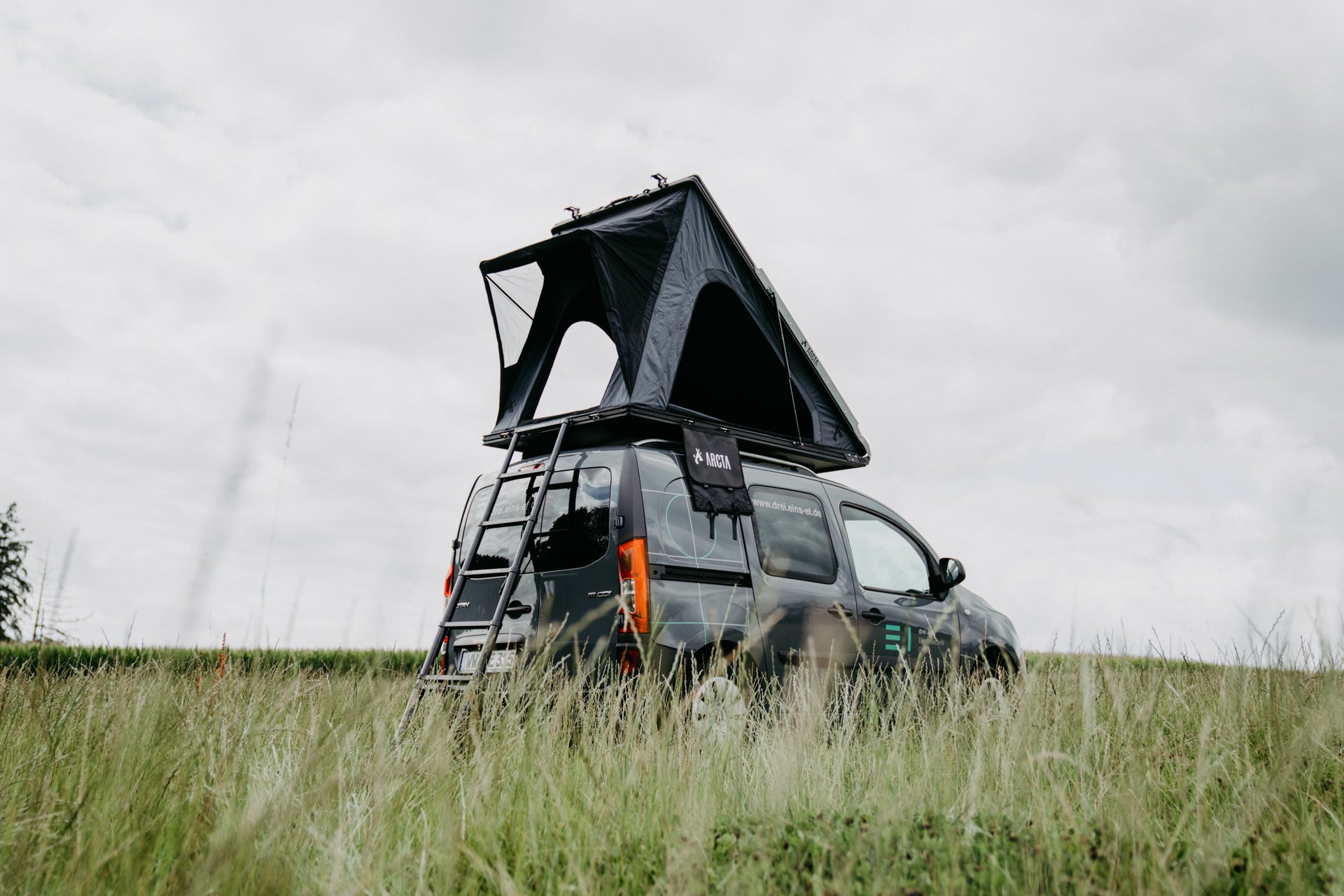 ARCTA Dachzelt auf Mini-Van auf einer Wiese bei bewölktem Himmel